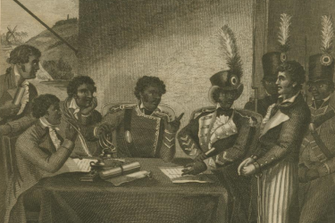 A group of men dressed in military uniform sit around a table, surrounded by soldiers carrying muskets who stand behind a white prisoner. One man is writing on a piece of parchment on the table.  